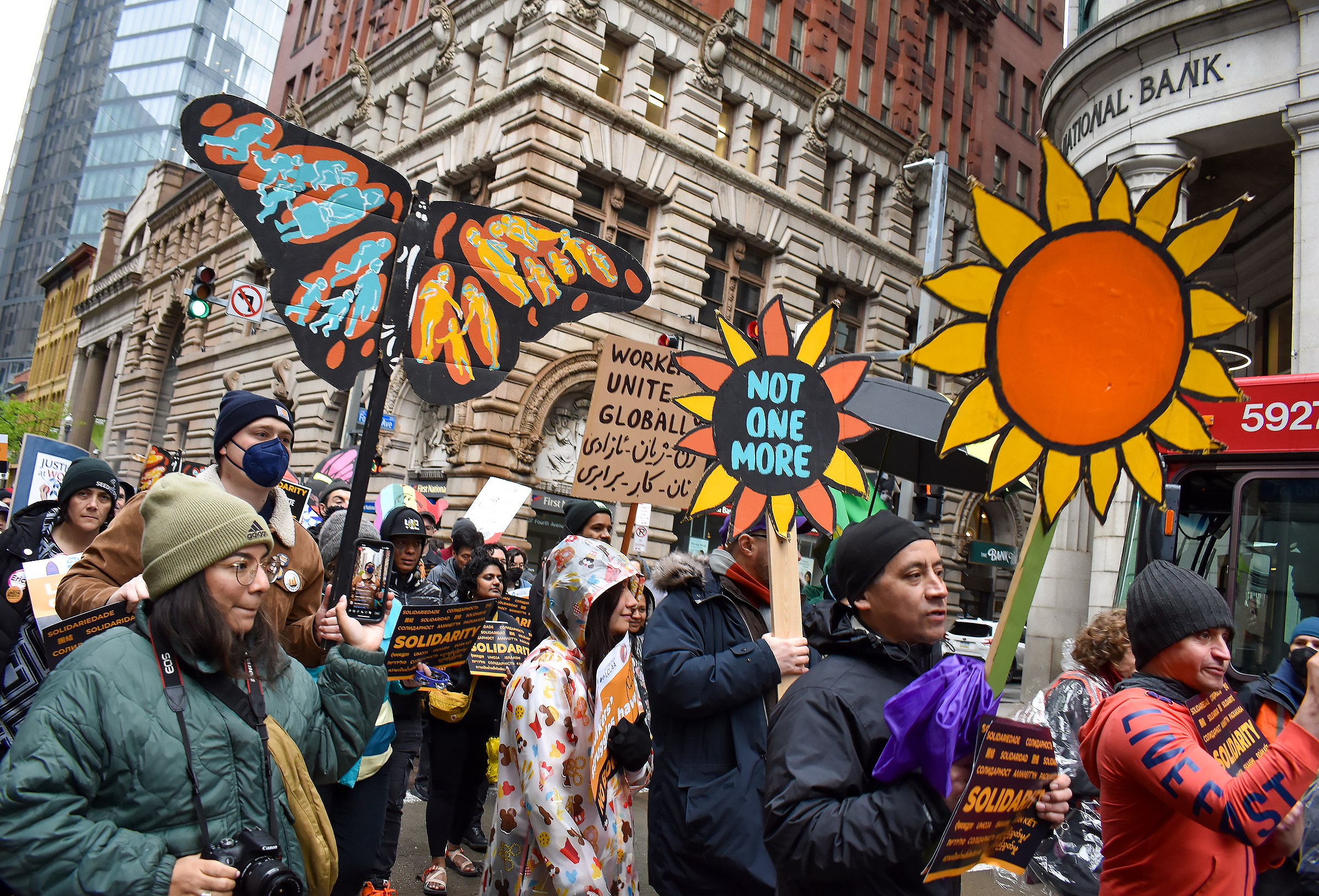People walk together in a street for a protest holding colorful signs like a butterfly and flower